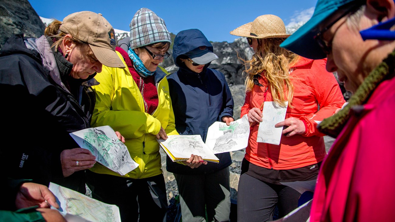 Several people gathered in a group holding drawings of coastal Alaska