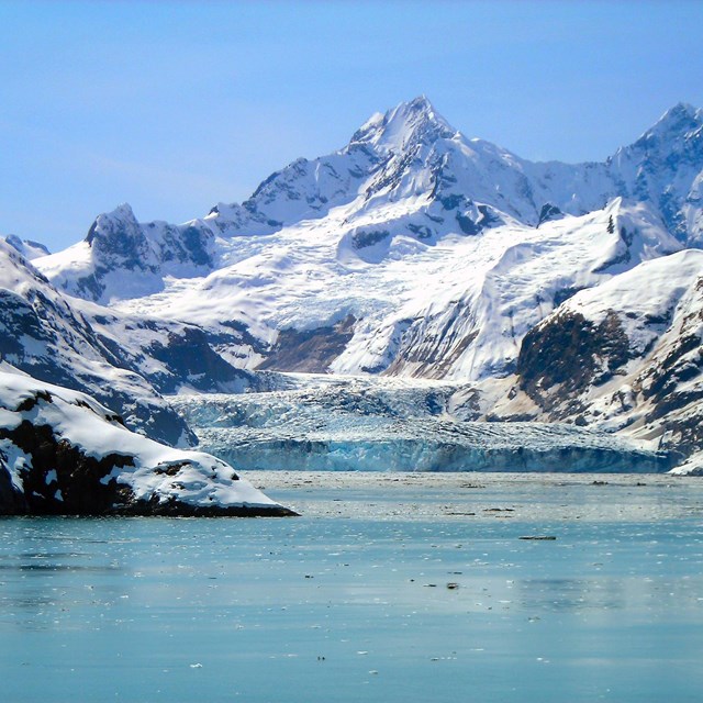 snow-covered mountain rising up with glacier and ocean in foreground