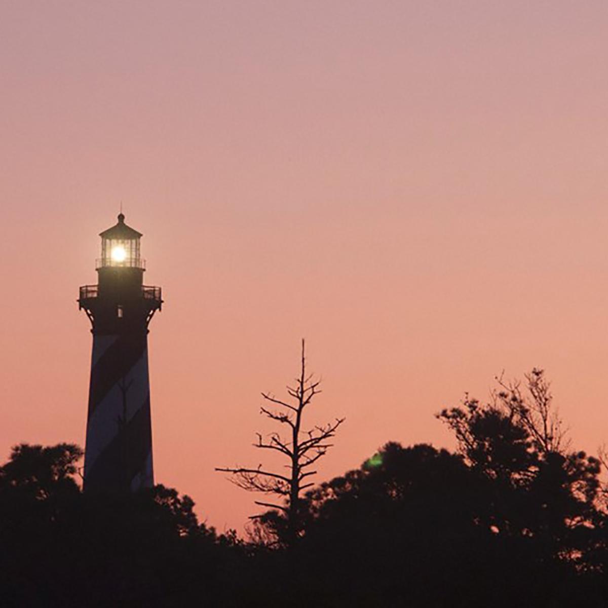 lighthouse at sunset with trees in the foreground