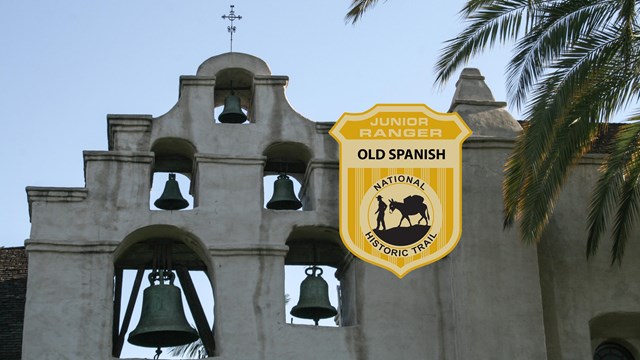 A junior ranger badge imposed upon an image of a white, spanish style mission, close up on the bells