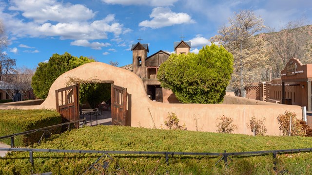 Historic adobe church in a desert setting with lush landscaping.