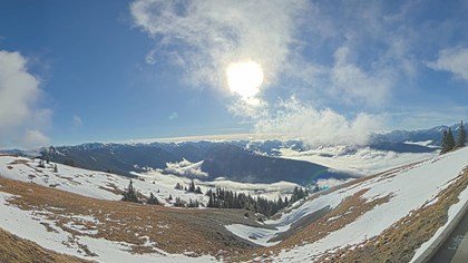 Mountain panorama under sunny skies, and a foreground hillside with patchy snow.