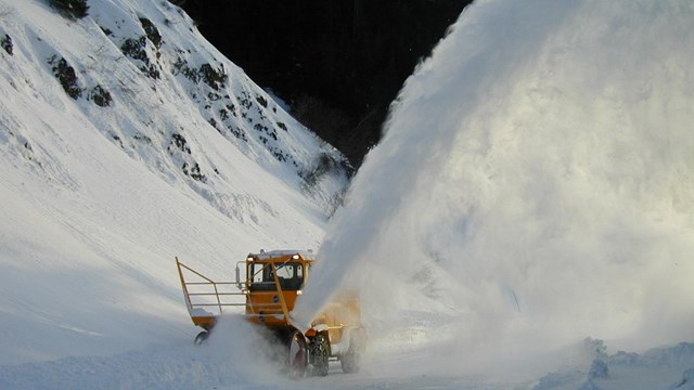 Snow plow blows snow up and out of the way.
