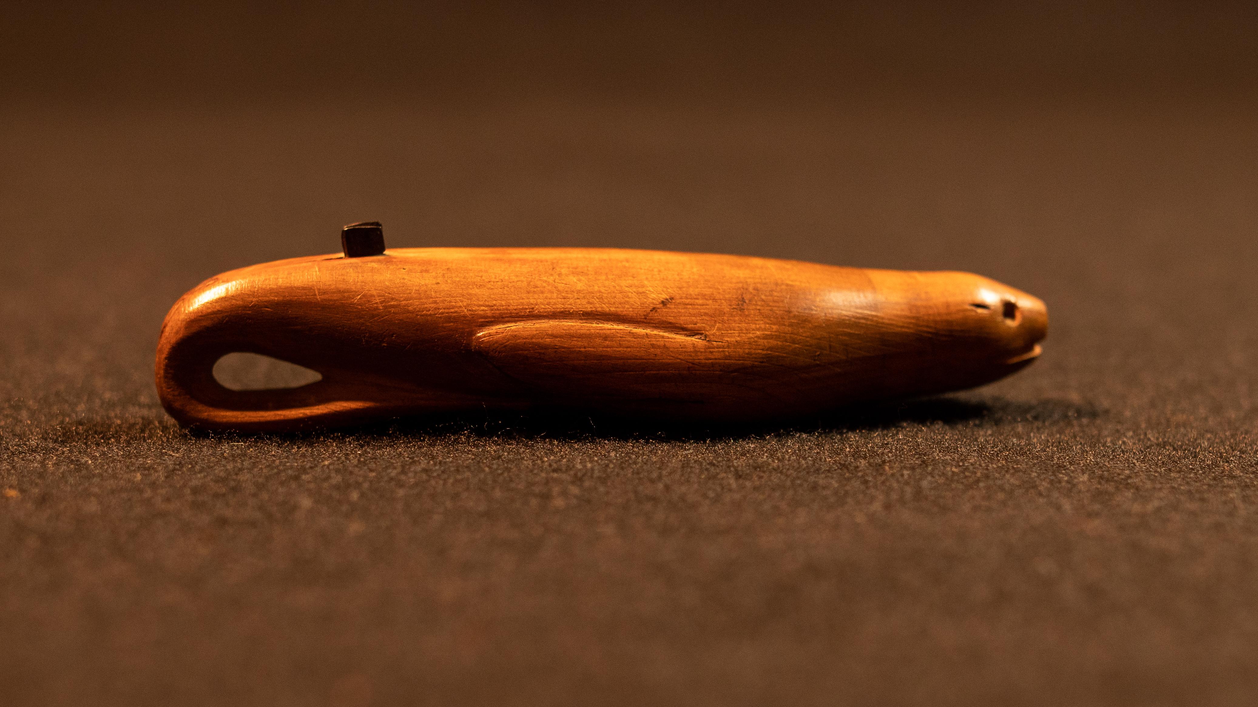 A small wooden tool carved in the shape of a seal, with two small parallel metal blades on its back.