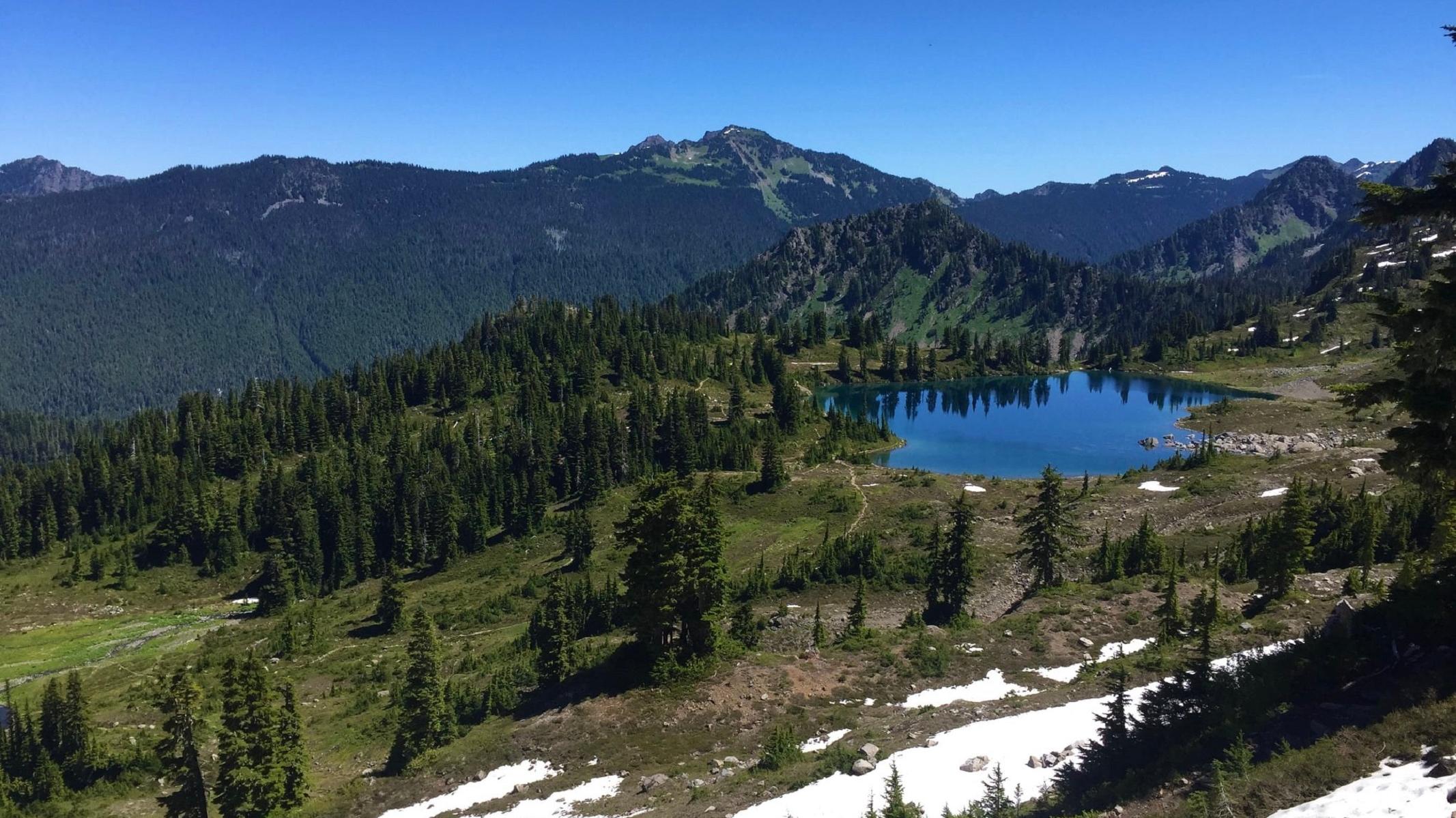 Mountains with some snow and a blue subalpine lake on a sunny day.