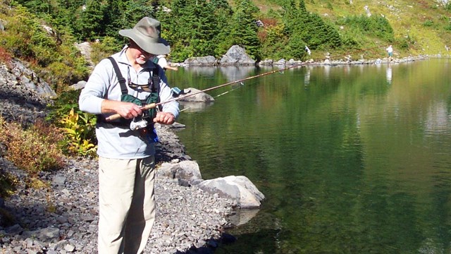 Man stands by lake with fishing pole.