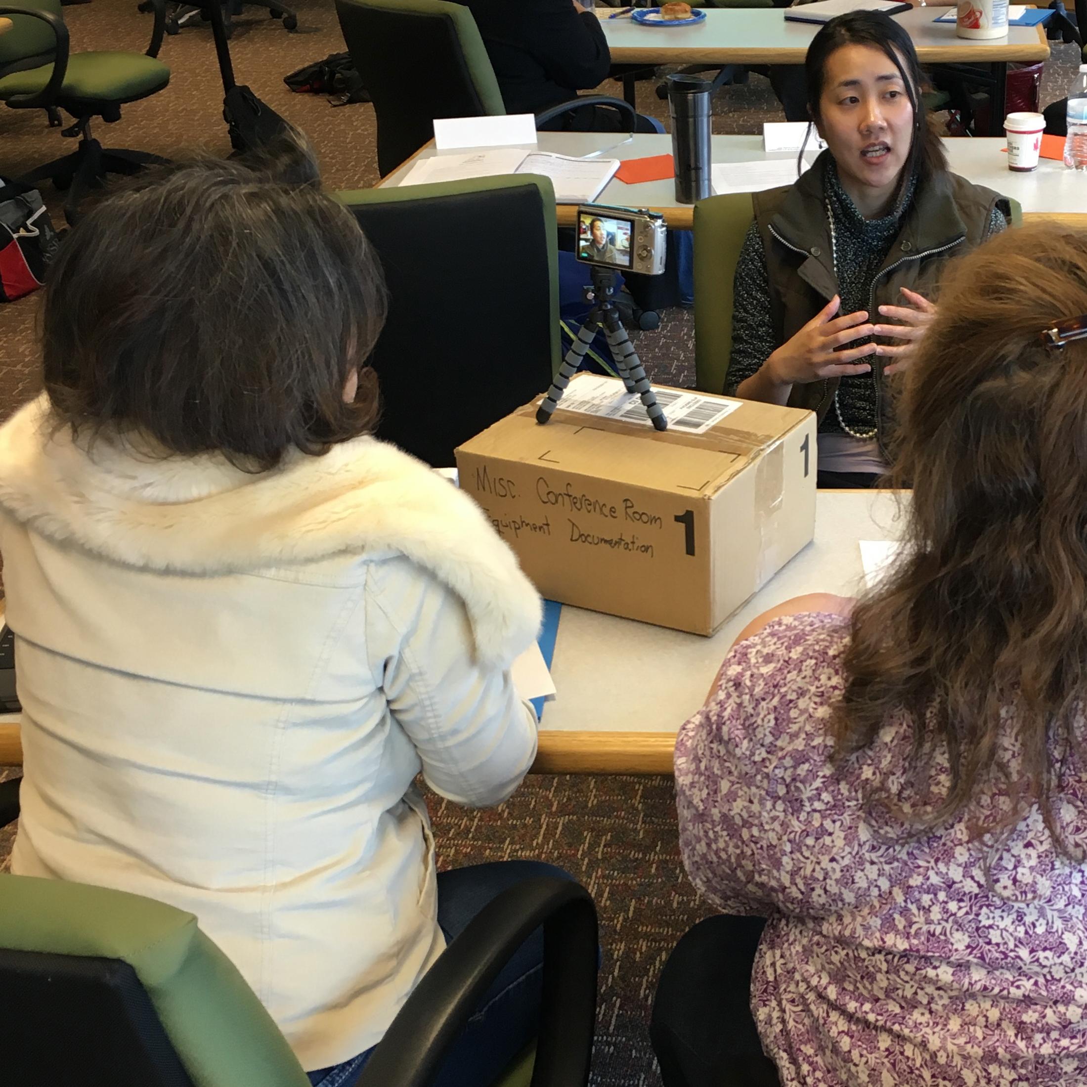 Three students at a table practice video recording interviews with each other during a workshop.
