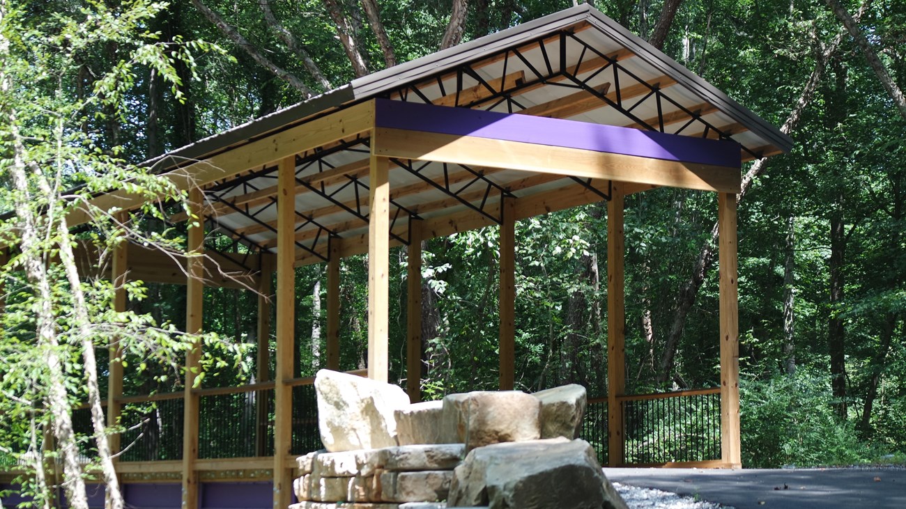 A metal covered bridge with purple details and a paved trail