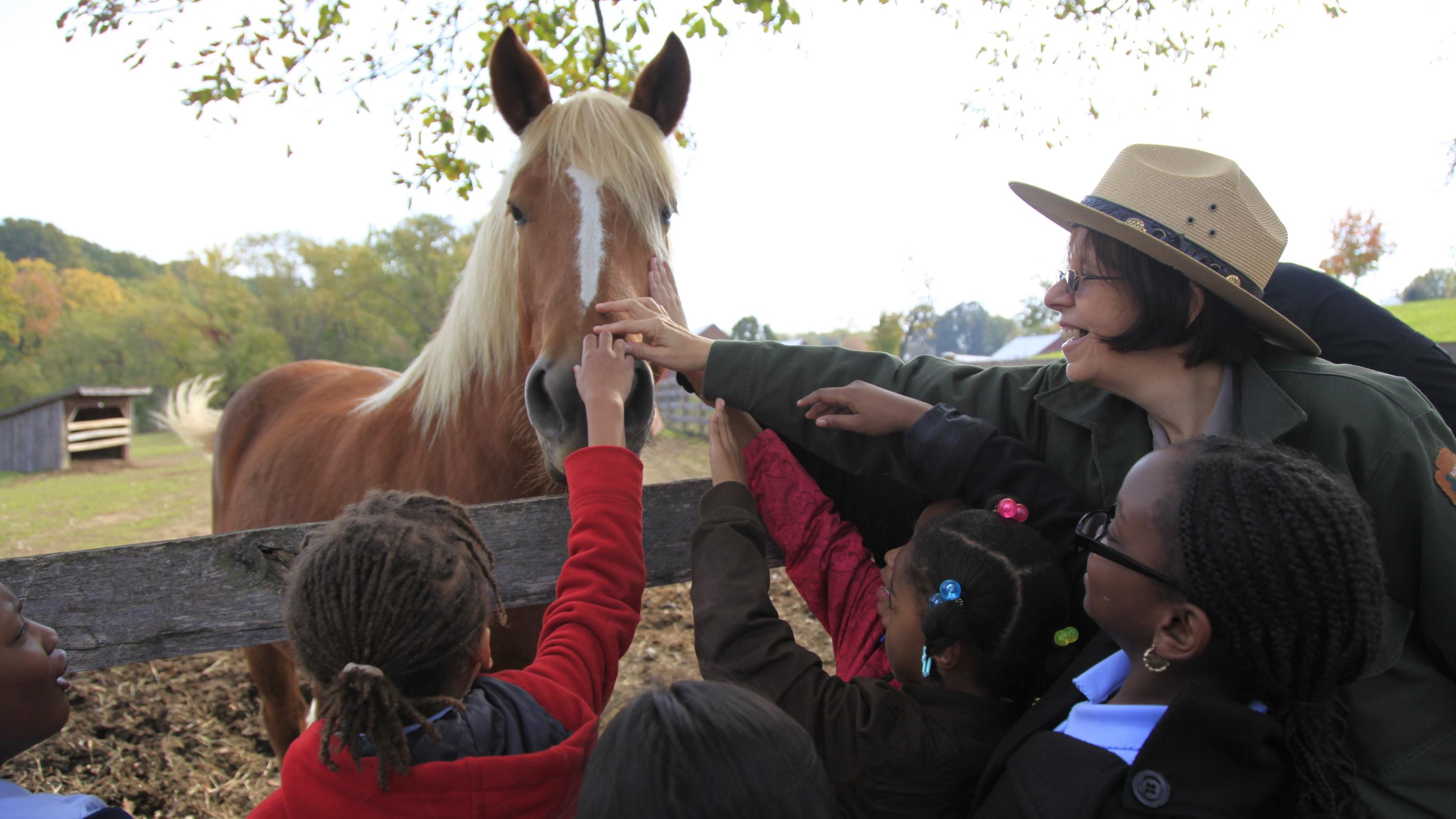 a park ranger with children petting the nose of a brown horse