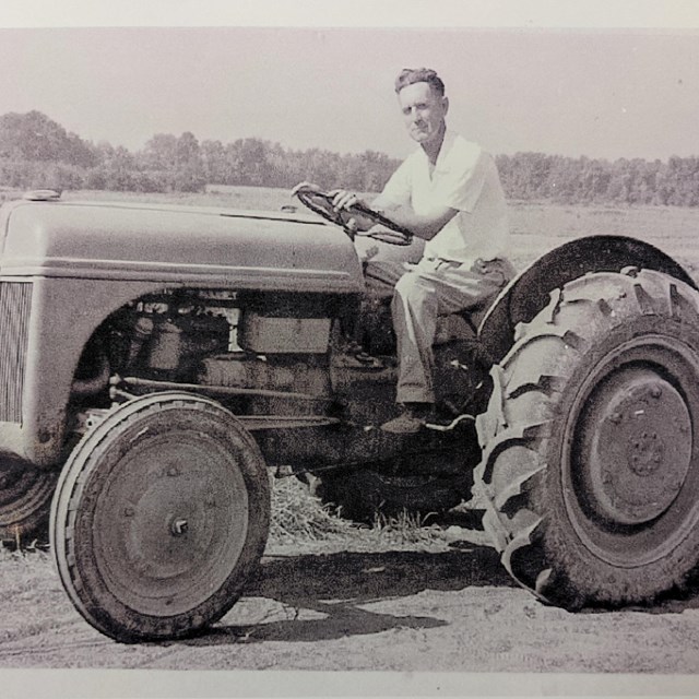 a black and white image of a white man on a tractor 