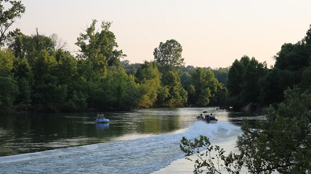 A motorboat drives past a raft on a river.