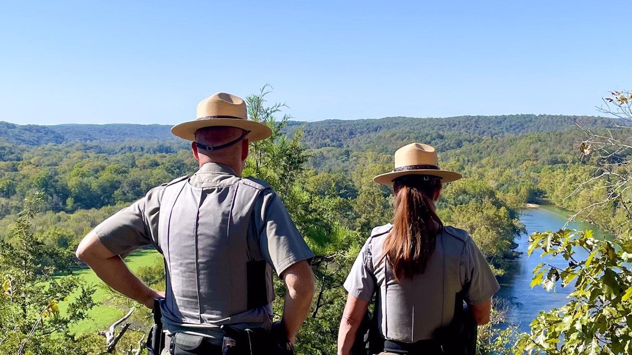 Two rangers stand on a bluff overlooking a river.