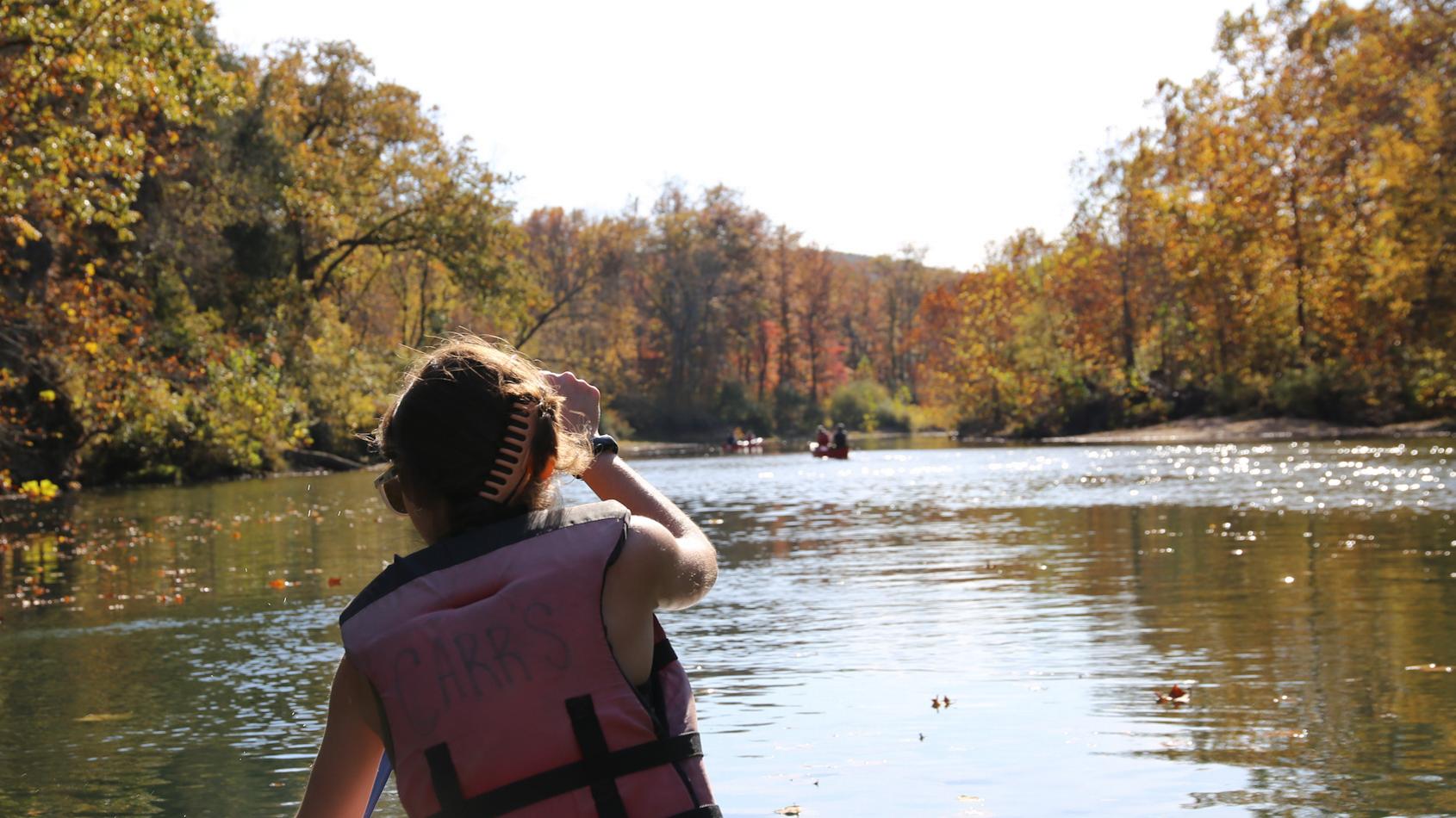 A woman in a personal flotation device paddles down a river.