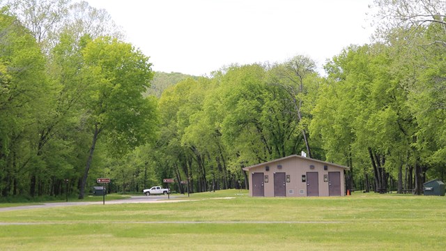 A restroom building stands at the end of a grassy field.