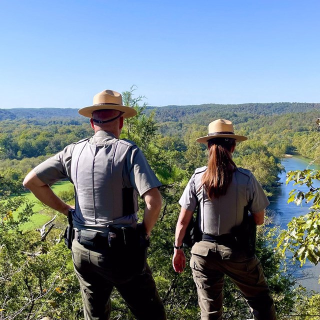 Two park rangers overlook the river from a cliff.