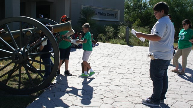 A Park Stewards Summer Intern and children standing at a cannon.