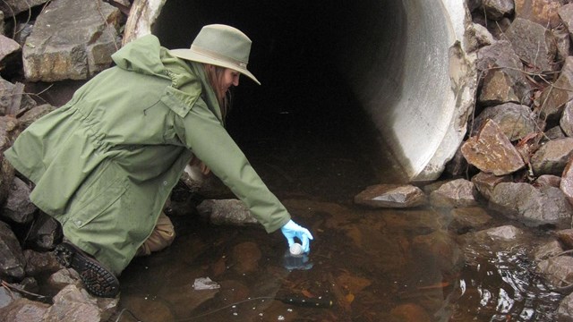 Hydrologic Technician collects a water sample for water quality monitoring.