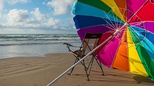A chair and colorful beach umbrella. 