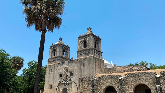 A historic Spanish mission with a palm tree in the front. 