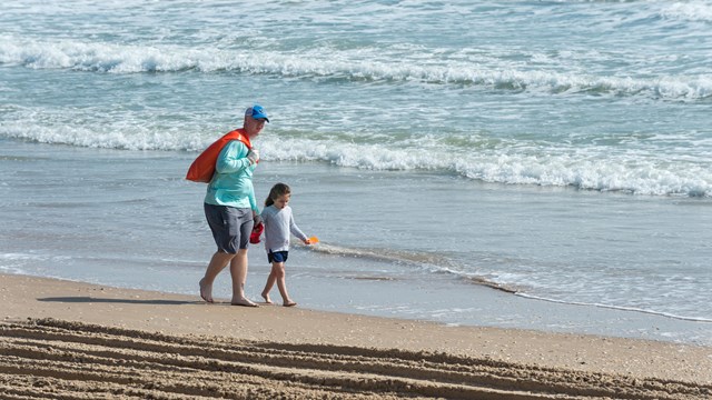 Two people walk on the beach a pick up trash.