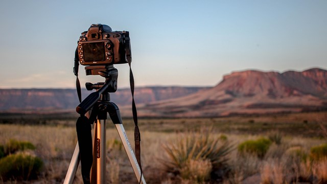 View of a camera on a tripod with mesas and cliff faces blurred in the background.