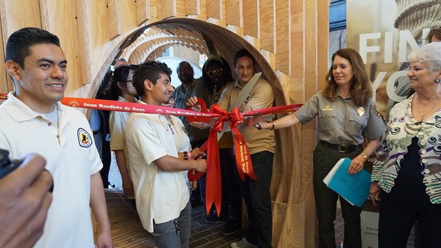 A student cuts a red ribbon while a ranger assists.