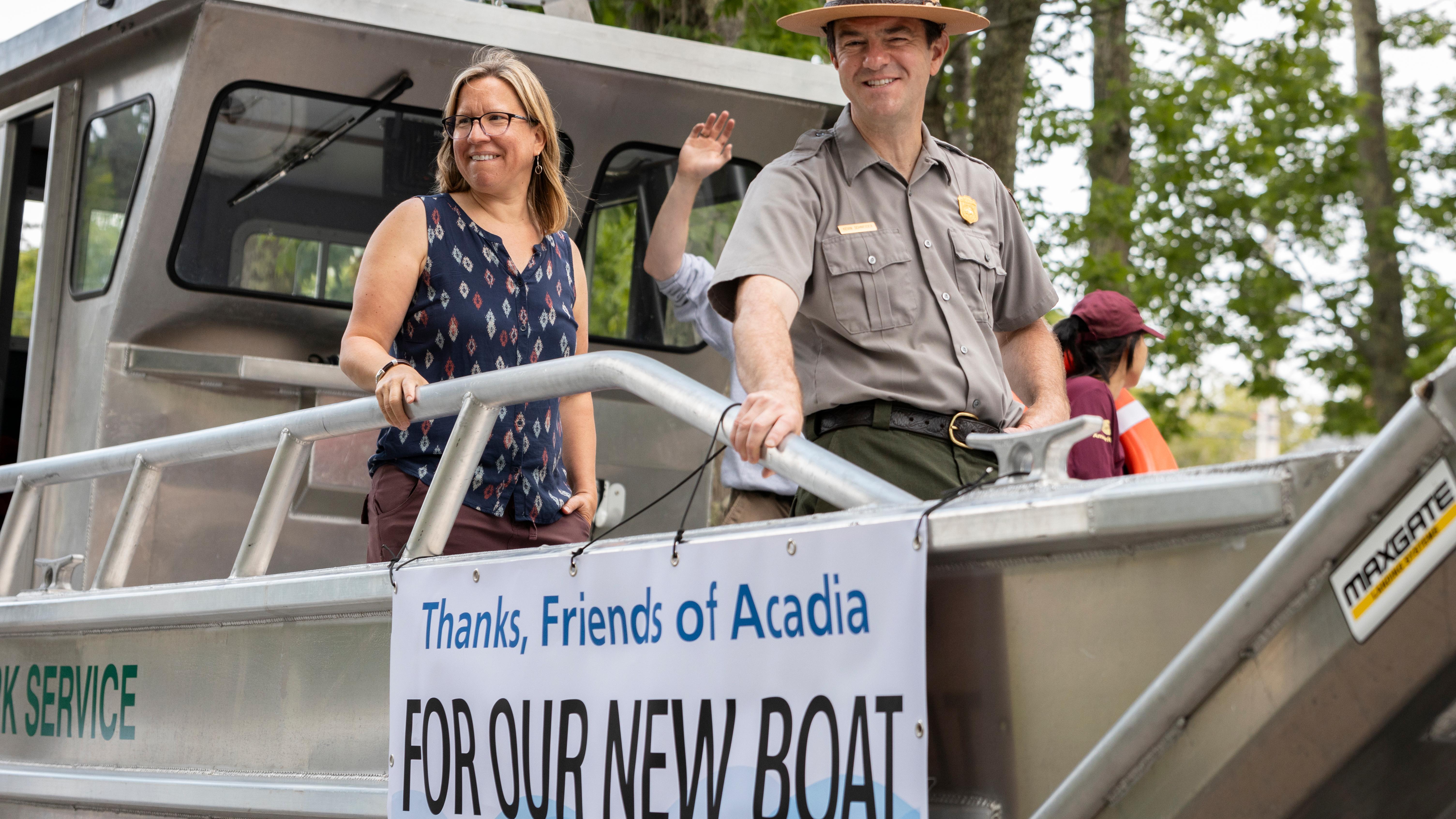 Two people stand on a new boat with a banner reading "Thanks, Friends of Acadia FOR OUR NEW BOAT."
