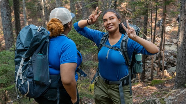 A female Student Conservation Association participant holds two peace signs to the camera.