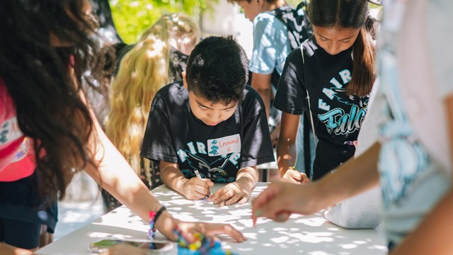 A young child draws on paper at a craft table for button making.