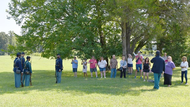 A crowd of people watch a four black men dress in US Civil War Uniforms