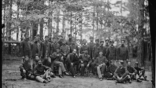 Two lines of soldiers in a group photo in a wooded area. 