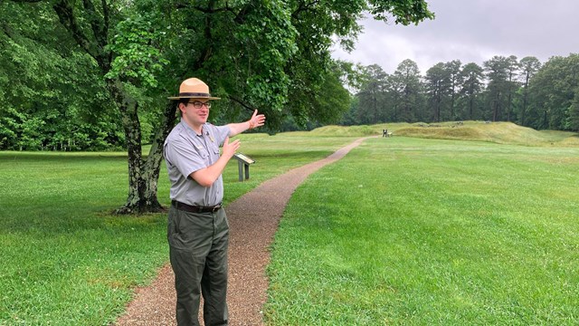 White man in NPS uniform points at earthworks