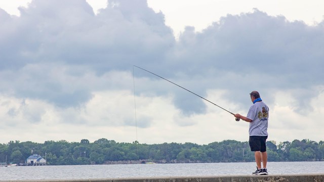 Man standing on a wall with a fishing pole cast into Lake Erie with ominous clouds 