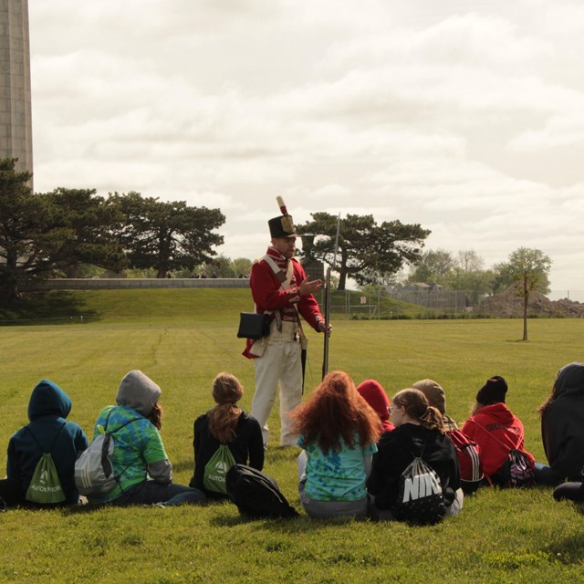 Man in historic military uniform talks to a groups of children