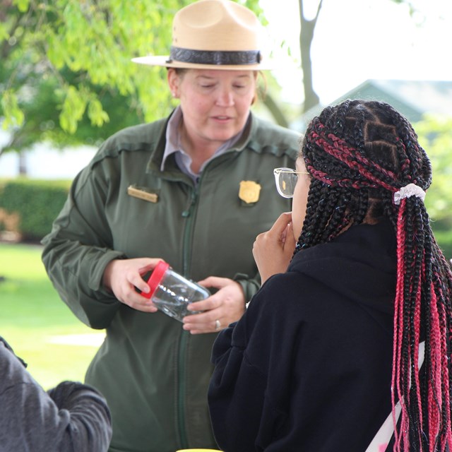 A park ranger holds a jar while talking to children.