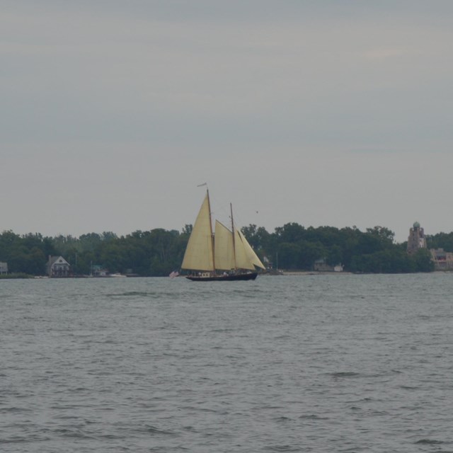 A sailing ship on the water with land behind.