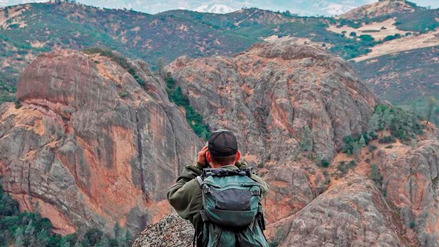 Biologist uses binoculars to look out over the geologic formations of Pinnacles.