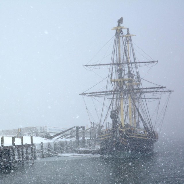 a wharf with tall ship on right; snowing