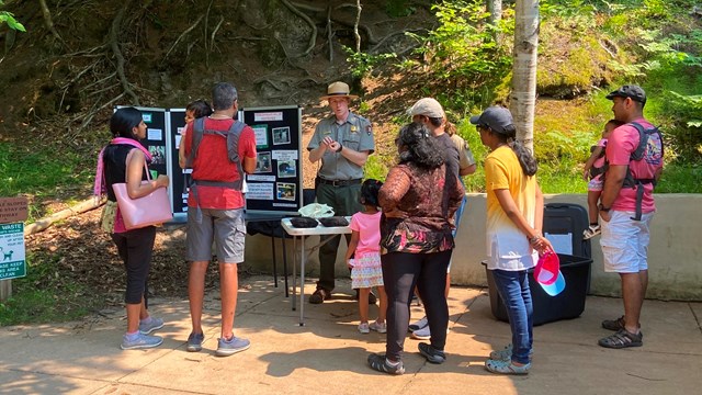 A group of people gathers around a ranger program table on a sunny day.