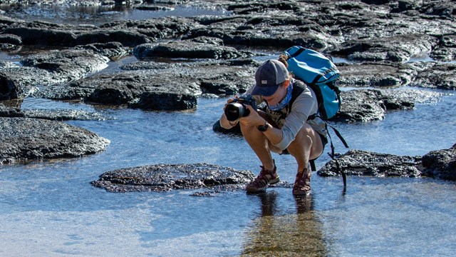 A photographer crouches on rocks and water. 