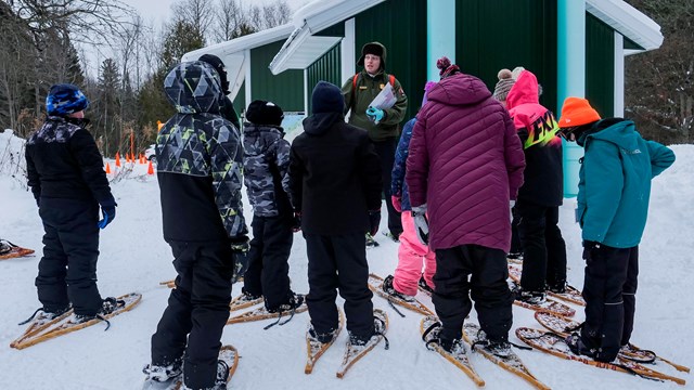 A ranger talks with a group of schoolkids on snowshoes.