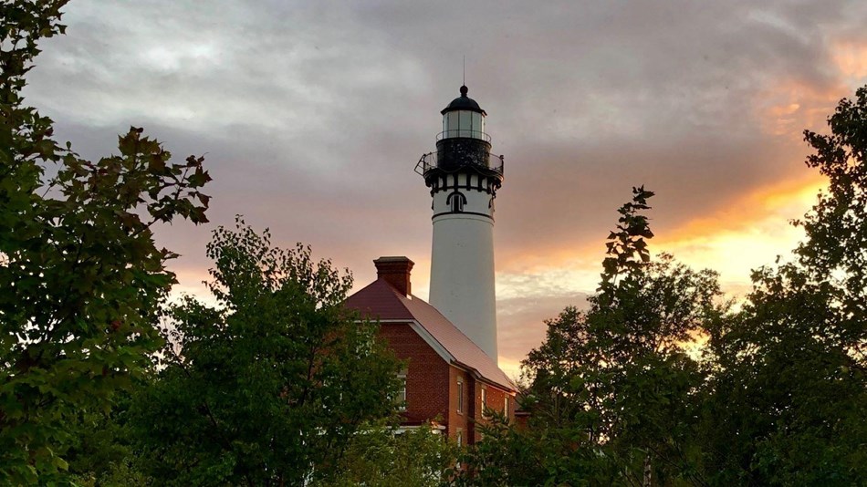The Au Sable Light Station through shrubs and trees at sunset.