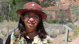 A young girl stands in front of a fort wearing dozens of Junior Ranger badges.