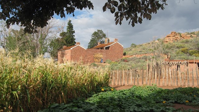 A sandstone fort, red cliffs, and garden plants in front of a cloudy sky