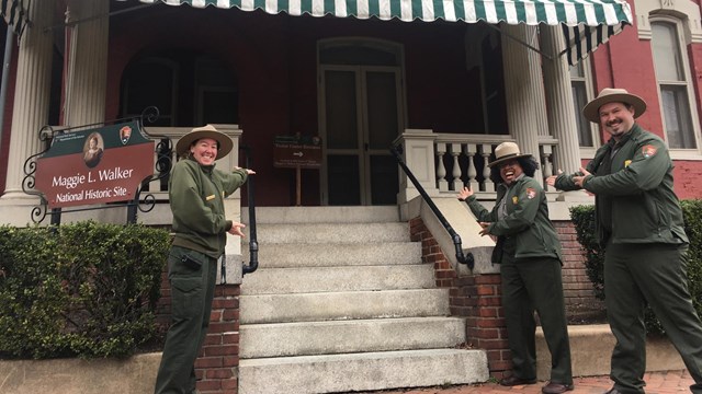 rangers gesture welcomingly to the front of a historic house