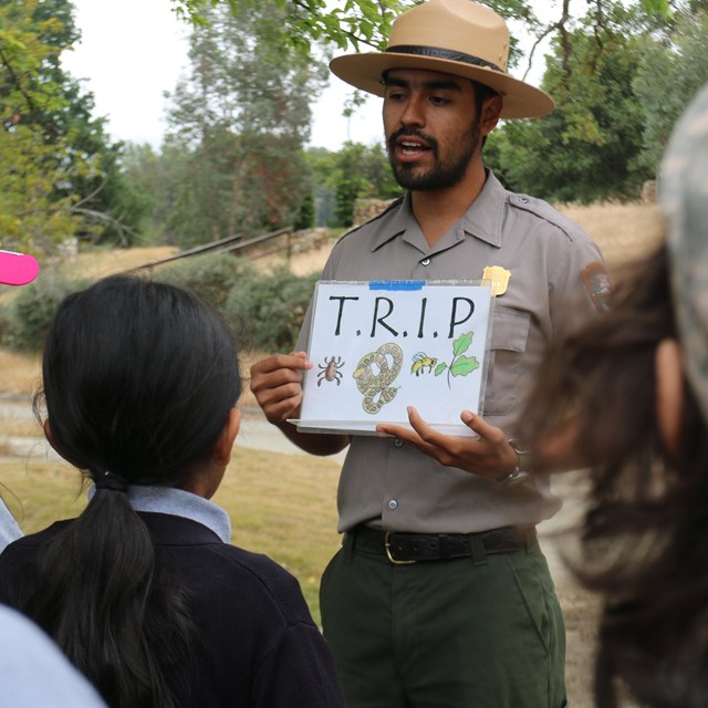 Park ranger talking to a group while holding a sign that reads 