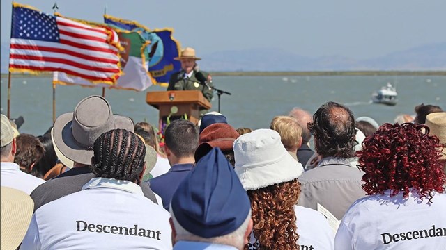 Seated crowd faces a Park Ranger at a lectern. 