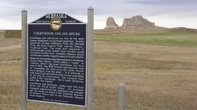 A large sign stands in front of a distant rocky bluff.