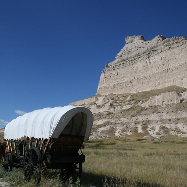 A wagon replica with fiberglass oxen in front of a large stone bluff.