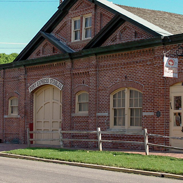 A large, one-story red brick stables with cream colored doors.